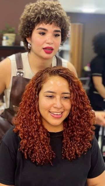 Estilista detrás de una clienta con rizos cobrizos