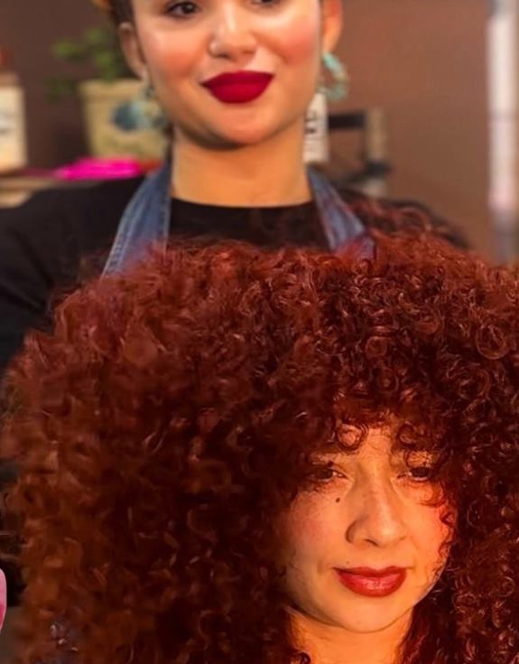 Clienta con un gran afro cobrizo definido junto a su estilista